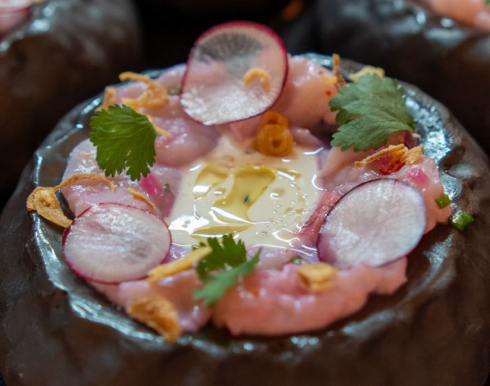 Salmon crudo with radish and kumquat in a black bowl