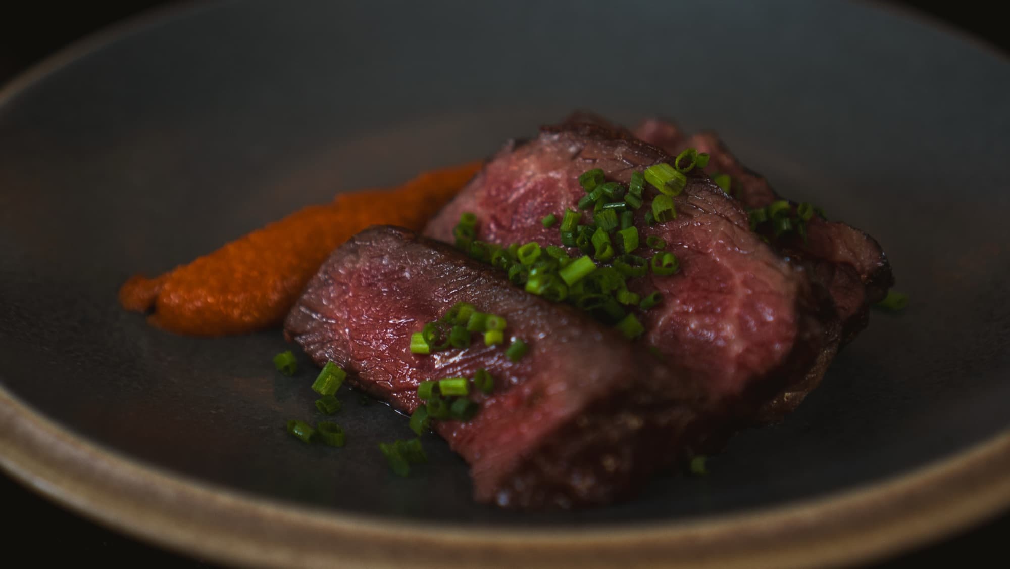 Seared beef with romesco and chives on a stone plate